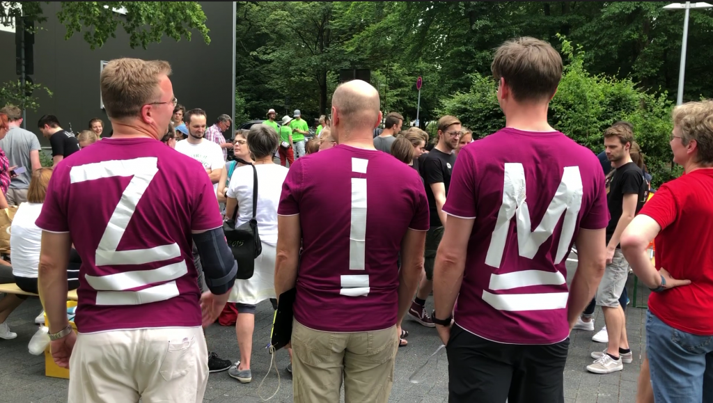 3 Personen von hinten fotografiert - auf den Rücken Buchstaben aufgeklebt