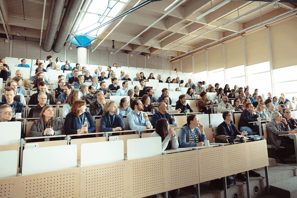 Foto eines Hörsaals. Die Reihen sind mit Teilnehmenden des Hochschultreffens gefüllt. Diese Blicken entspannt nach vorne.